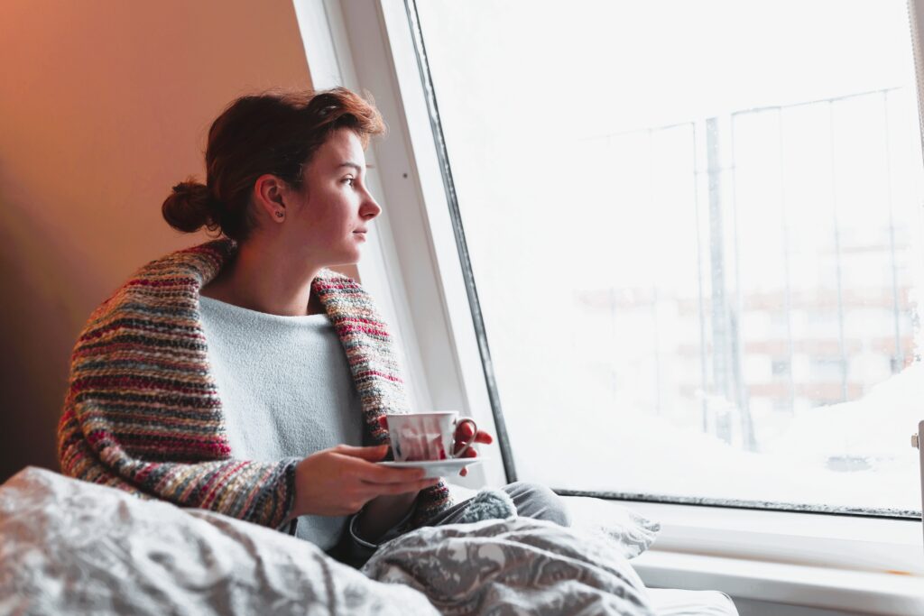 Frau mit einer Tasse Tee am Fenster als Symbol für Ruhe bei Reizdarm und stressbedingten Kopfschmerzen 